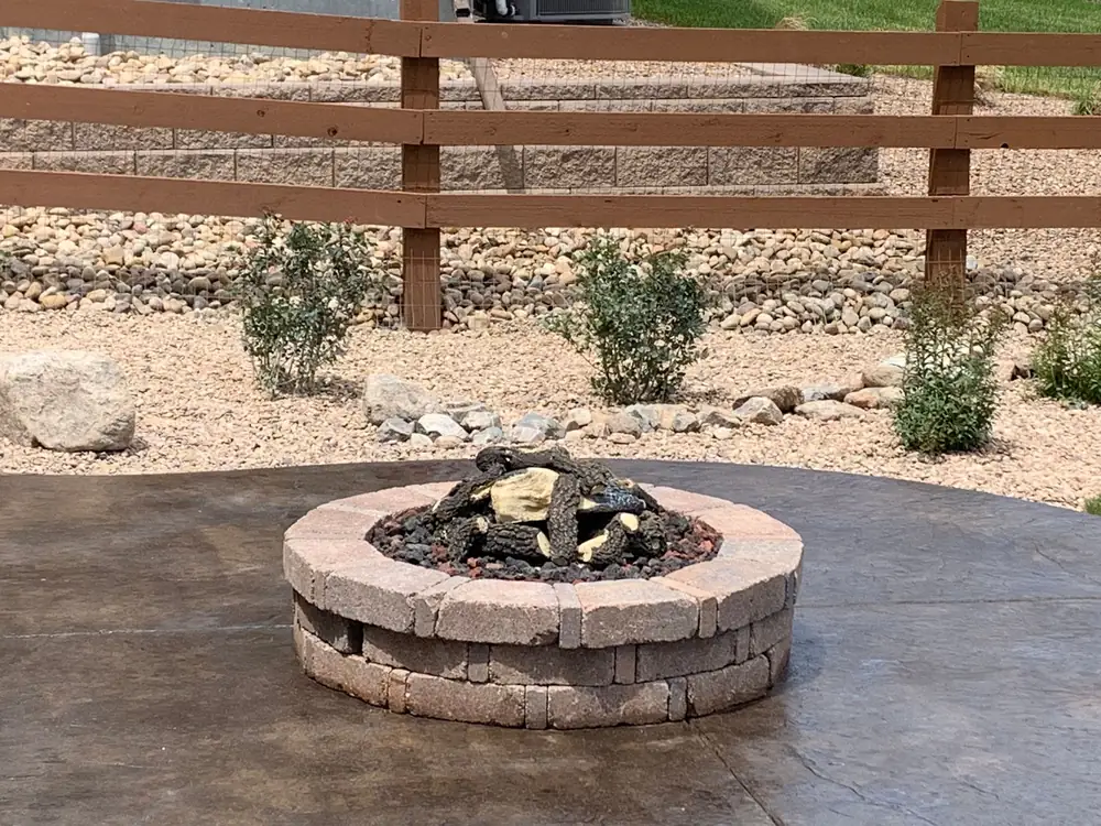 Round fire pit on a stained concrete patio with a xeriscape border