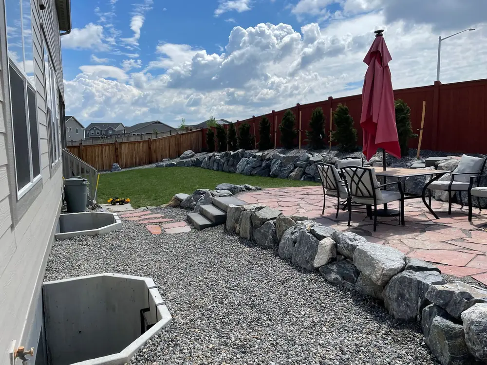 Flagstone patio held up by a boulder wall, with a gravel side yard