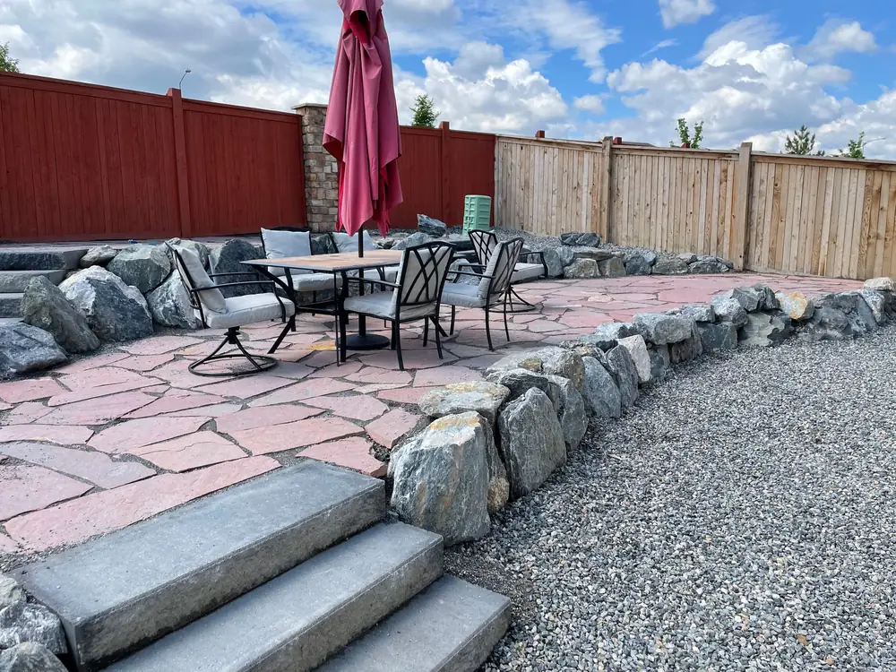 Stone slab steps leading up to a flagstone patio set behind boulders