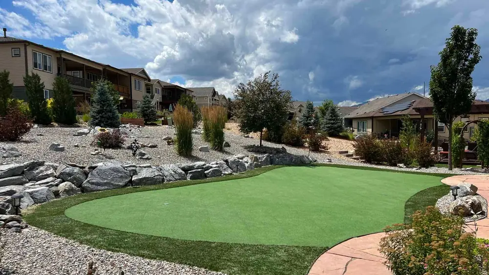 Artificial putting green framed by boulders, gravel beds, ornamental grasses and a flagstone path