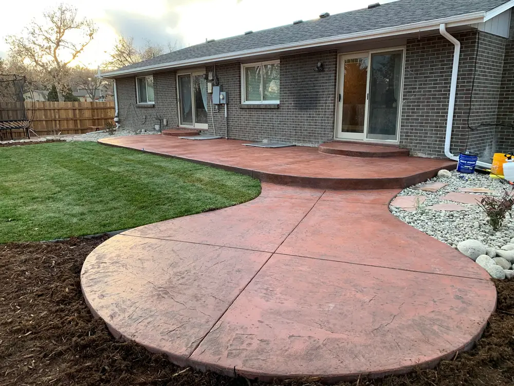 Curved red stamped concrete patio with a river rock bed and new sod