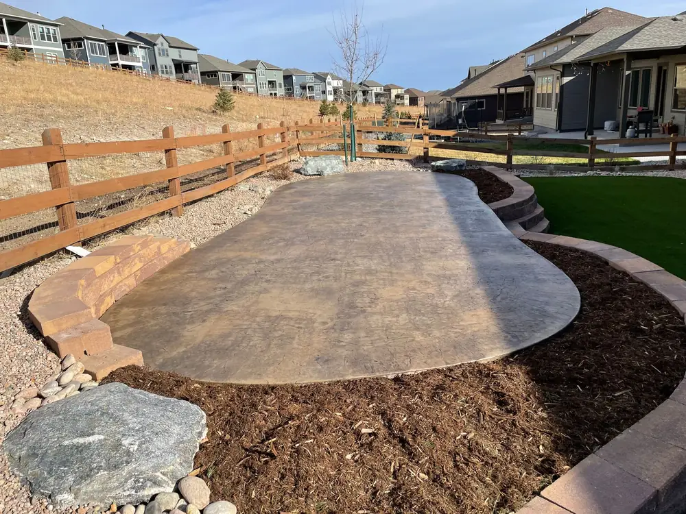 Wide stamped concrete path with mulch beds, boulders and a split rail fence